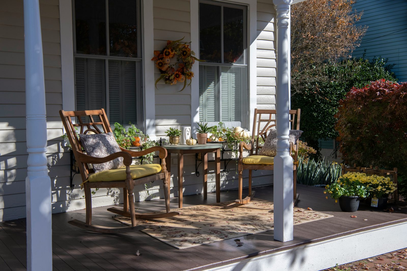 A welcoming covered front porch with wooden chairs, a small table and potted flowers